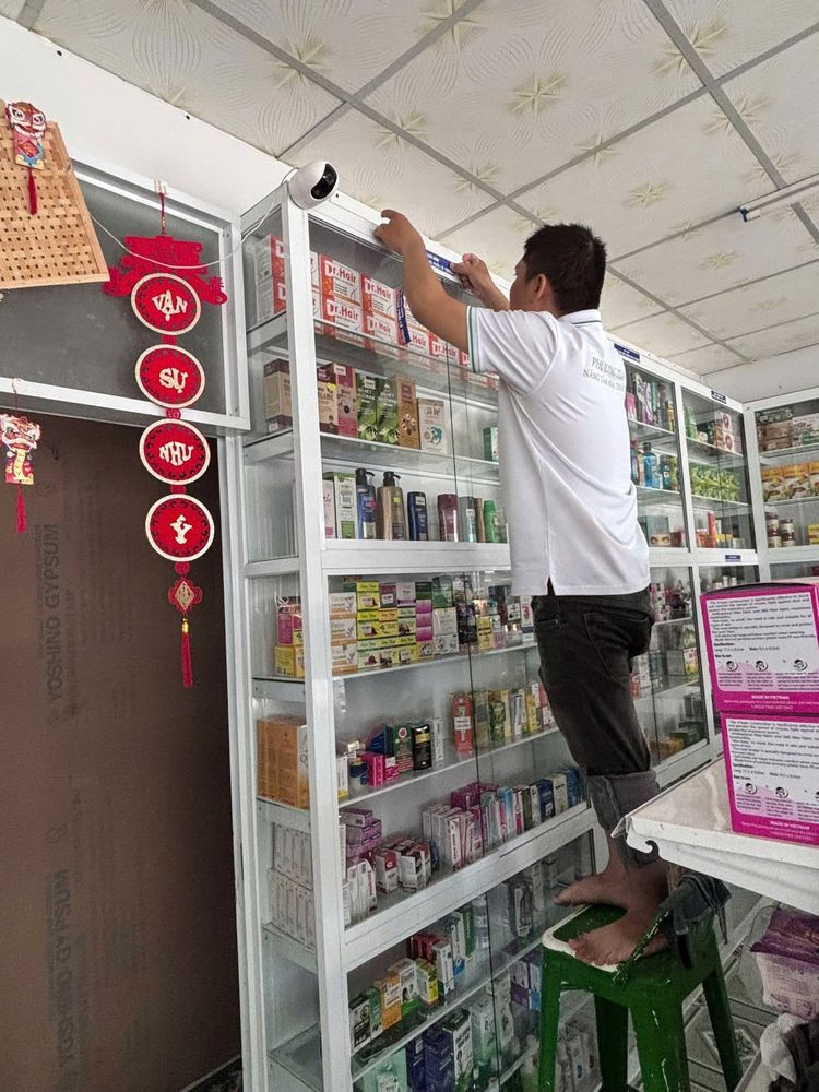 Nhân viên đứng trên ghế sắp xếp thuốc trên tủ cao